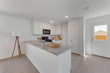 Kitchen with light wood-type flooring, black appliances, white cabinetry, and light stone counters