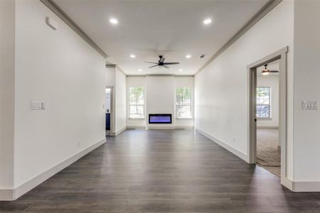 Unfurnished living room with a healthy amount of sunlight, crown molding, dark wood-type flooring, and ceiling fan