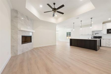 Kitchen with a kitchen island with sink, light hardwood / wood-style flooring, decorative light fixtures, a raised ceiling, and white cabinets