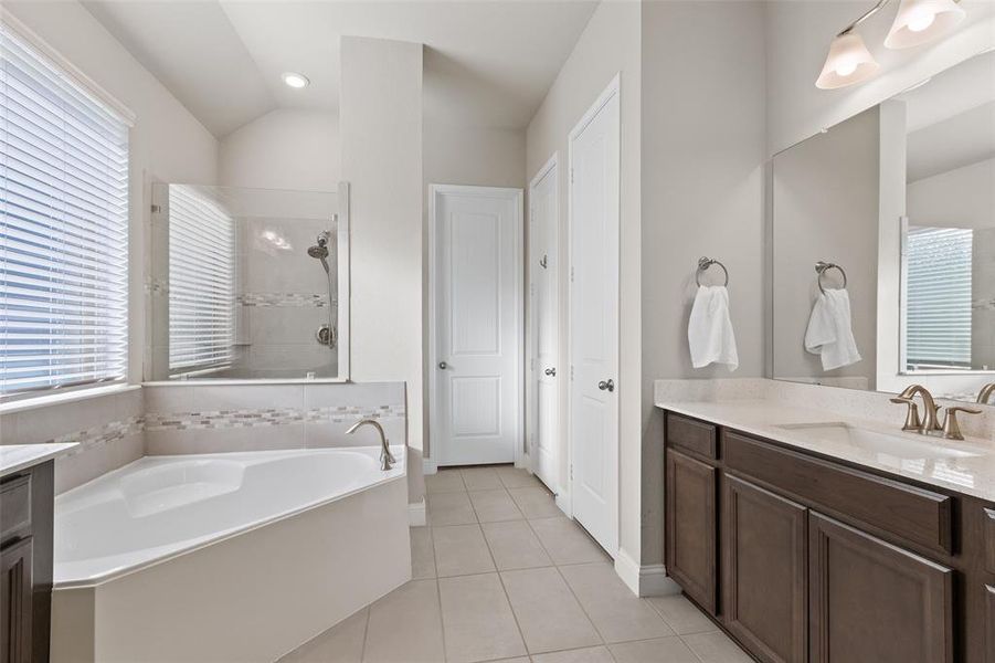 Experience spa-like luxury in the ensuite bathroom, featuring a deep soaking tub, a shower with a built-in bench, and a dual vanity area.