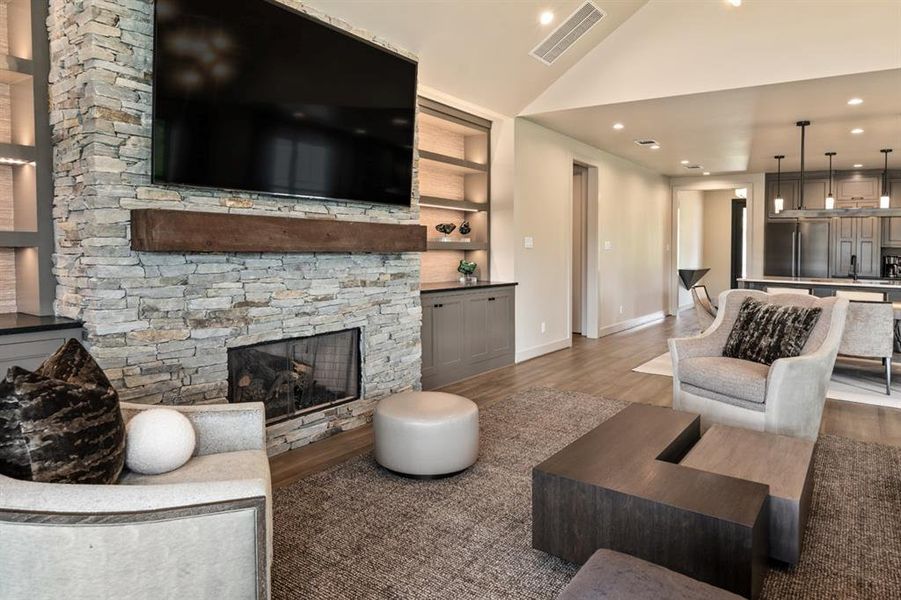 Living room with lofted ceiling, hardwood / wood-style flooring, built in shelves, and a stone fireplace