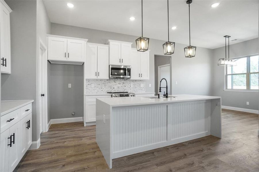 Kitchen with sink, dark hardwood / wood-style flooring, backsplash, and an island with sink