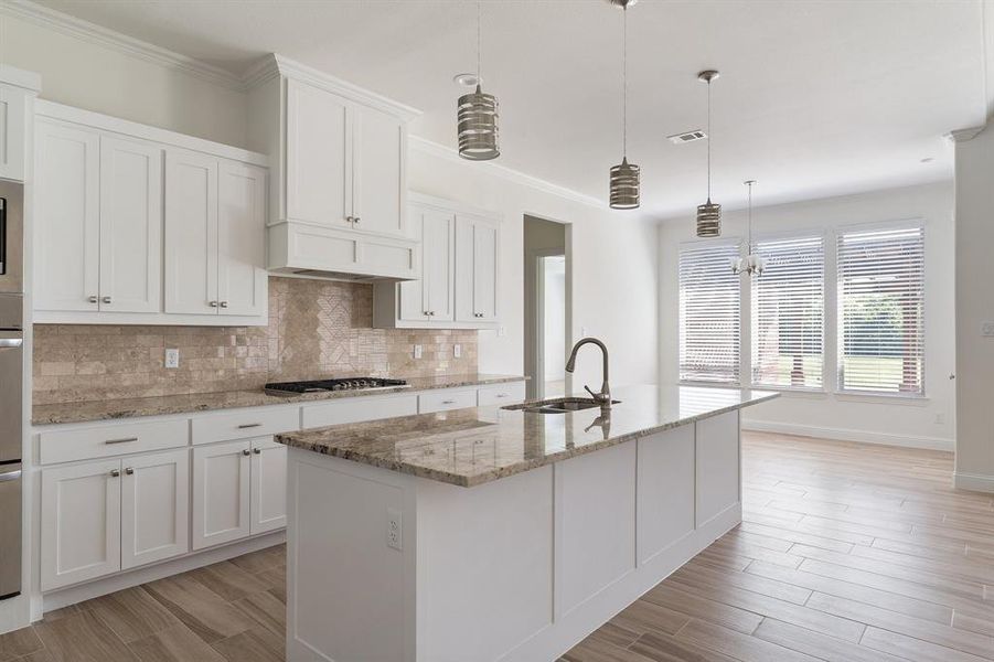 Kitchen with white cabinets, backsplash, an island with sink, sink, and ornamental molding