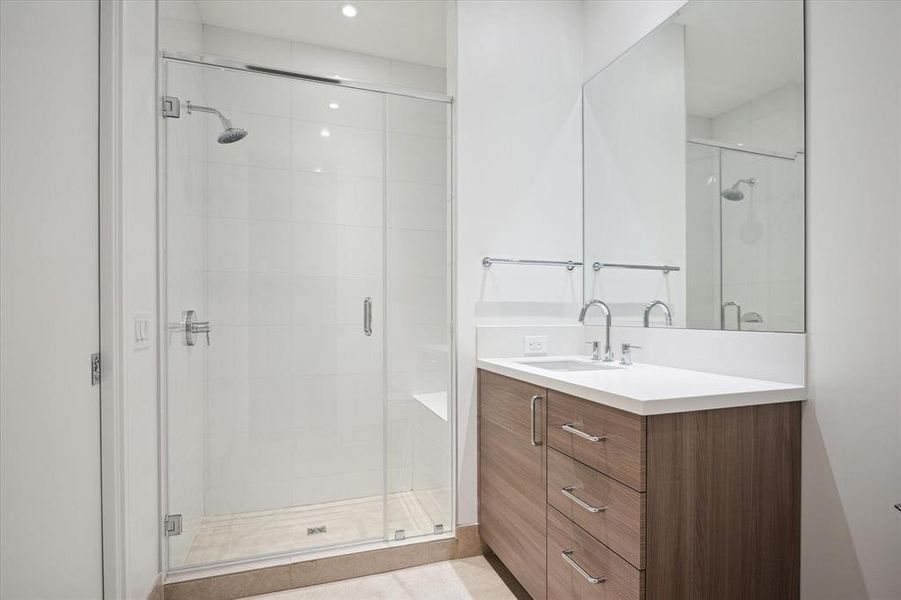 Secondary full bathroom has a glass-enclosed walk-in shower and a sleek vanity with a large mirror, offering a clean design.