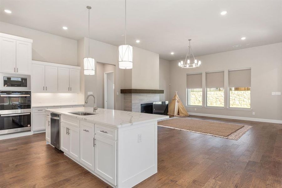 Kitchen featuring sink, decorative light fixtures, a center island with sink, white cabinetry, and dark hardwood / wood-style floors