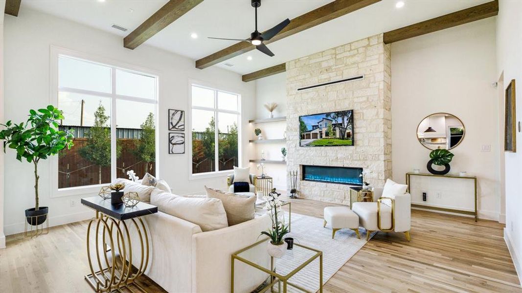 Living room featuring a stone fireplace, light hardwood / wood-style floors, beamed ceiling, and ceiling fan