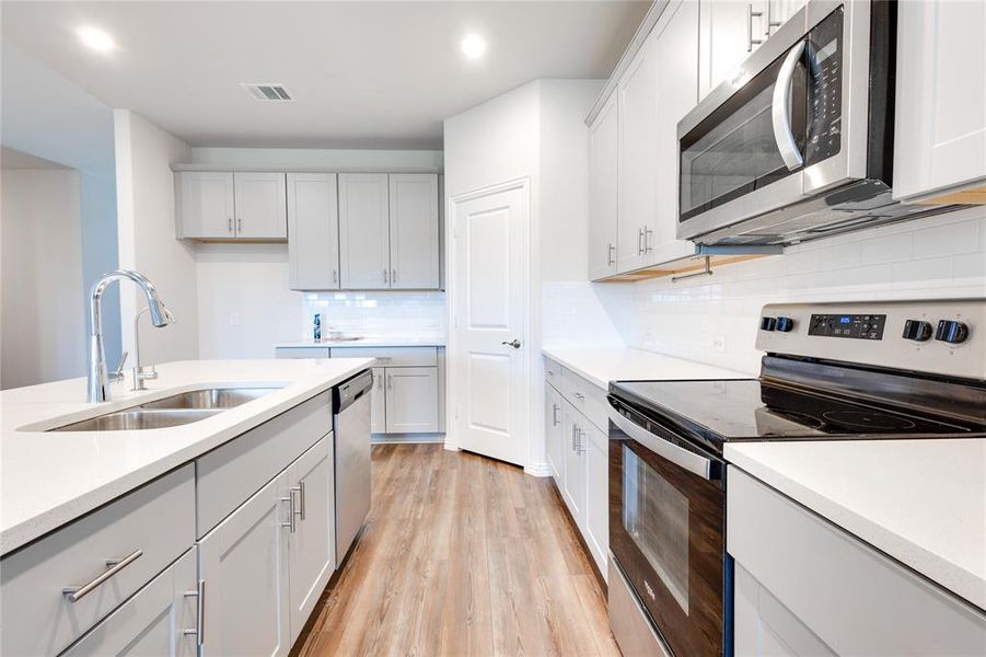 Kitchen with white cabinetry, tasteful backsplash, light wood-type flooring, sink, and appliances with stainless steel finishes