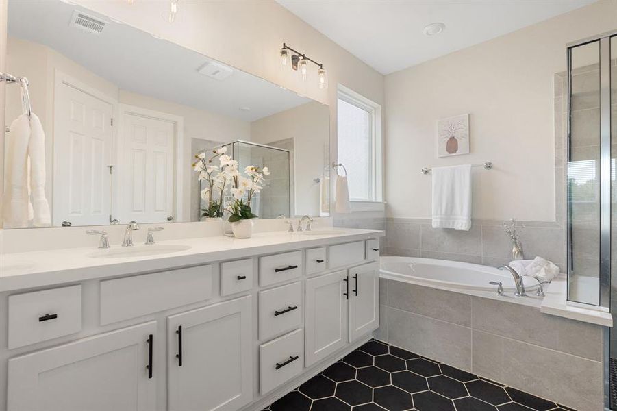 The luxurious primary bathroom features pristine white cabinets, quartz countertops and beautiful black floor and shower tiles.