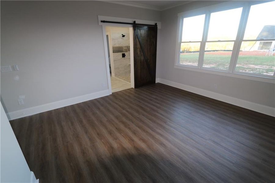 Empty room with a barn door, dark hardwood / wood-style flooring, and crown molding