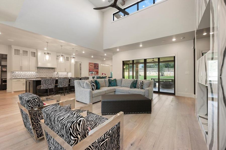 Living room with a high ceiling, ceiling fan, and light hardwood / wood-style floors