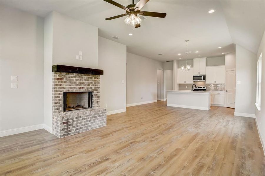 Unfurnished living room with ceiling fan, light hardwood / wood-style floors, vaulted ceiling, and a brick fireplace