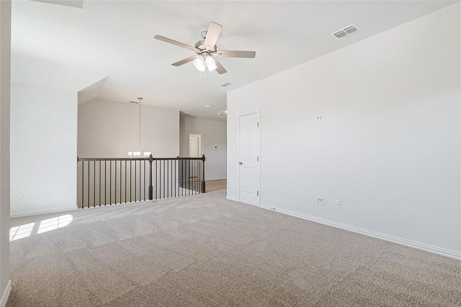 Carpeted spare room featuring ceiling fan with notable chandelier and lofted ceiling