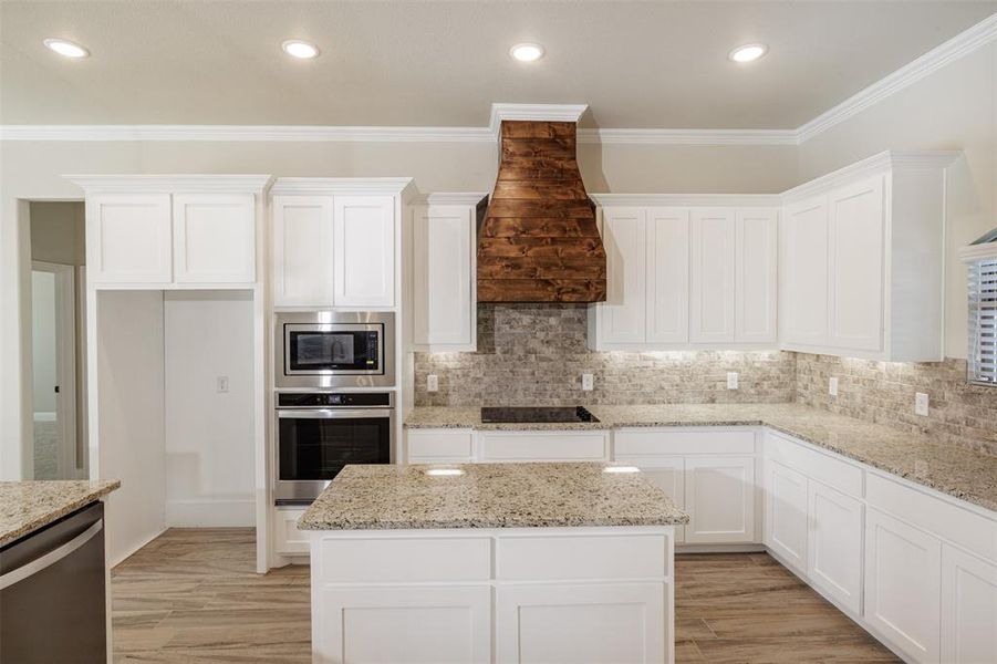 Kitchen with crown molding, custom exhaust hood, light hardwood / wood-style flooring, and stainless steel appliances