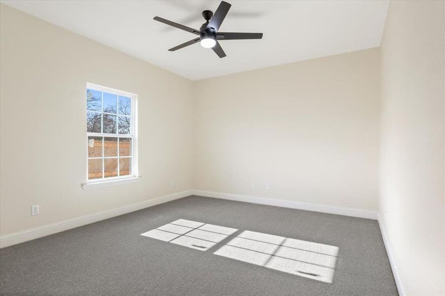 Empty room featuring a wealth of natural light, ceiling fan, and dark carpet