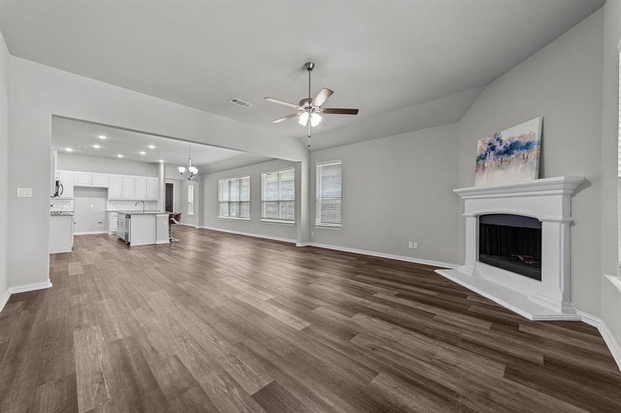 Unfurnished living room featuring ceiling fan with notable chandelier and dark hardwood / wood-style flooring