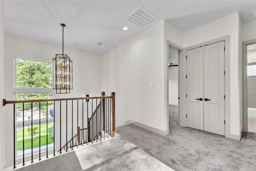 Upstairs View that leads you into the spacious game room,  gray carpet flooring throughout the 2nd floor and a view of trees through the window.