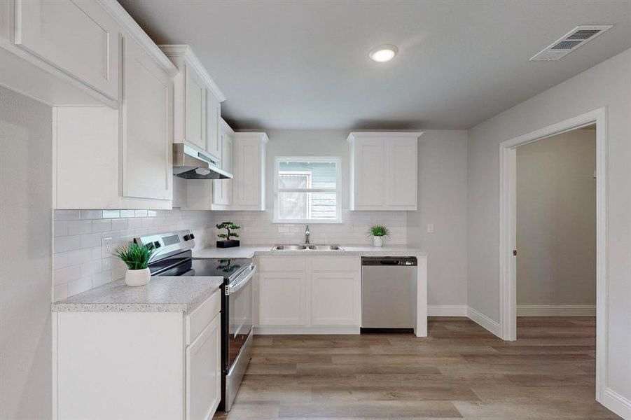 Kitchen with white cabinets, appliances with stainless steel finishes, light wood-type flooring, and sink