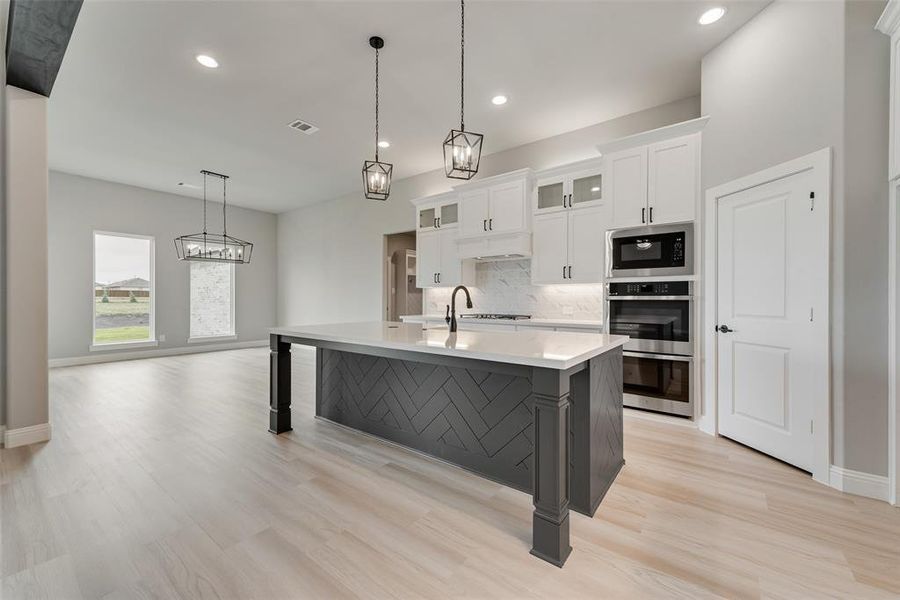 Kitchen with light wood-type flooring, white cabinetry, stainless steel microwave, and a kitchen island with sink