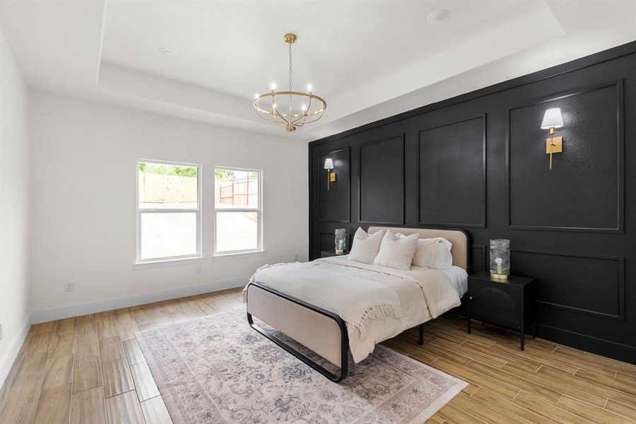 Bedroom with light hardwood / wood-style floors, a chandelier, and a tray ceiling