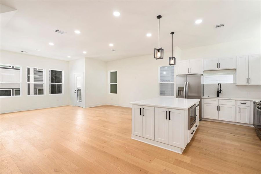 This is a spacious, modern kitchen with white cabinetry, premium stainless steel appliances, and a center island with storage and microwave, featuring recessed lighting, hardwood floors, and ample natural light from multiple windows.