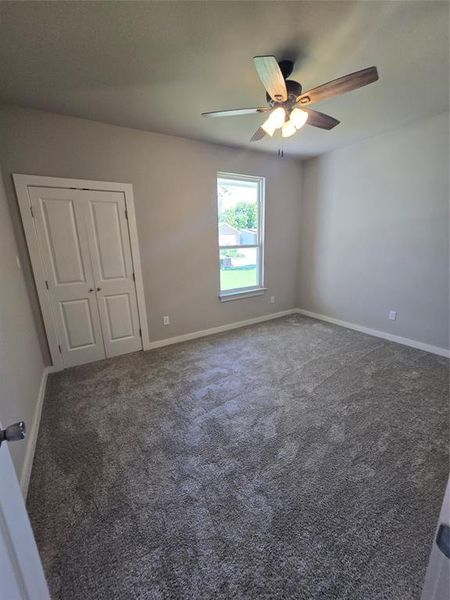 Empty room with ceiling fan and dark colored carpet