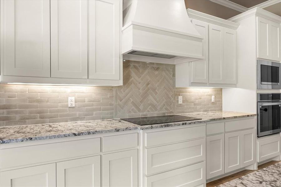 Kitchen featuring backsplash, white cabinetry, stainless steel appliances, custom exhaust hood, and light stone counters