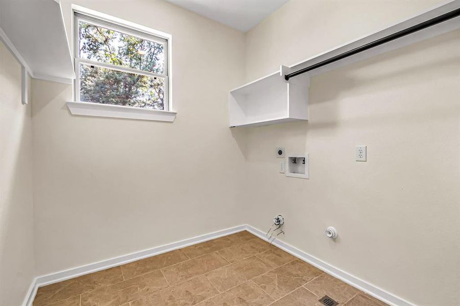 Laundry room is spacious and bright with hanging rod and storage shelves.