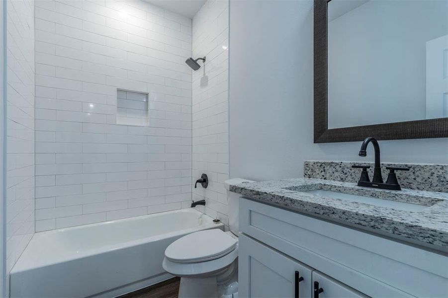 Full bathroom featuring hardwood / wood-style flooring, vanity, tiled shower / bath combo, and toilet