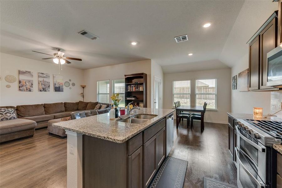 Kitchen with hardwood / wood-style flooring, stainless steel appliances, sink, light stone countertops, and a kitchen island with sink