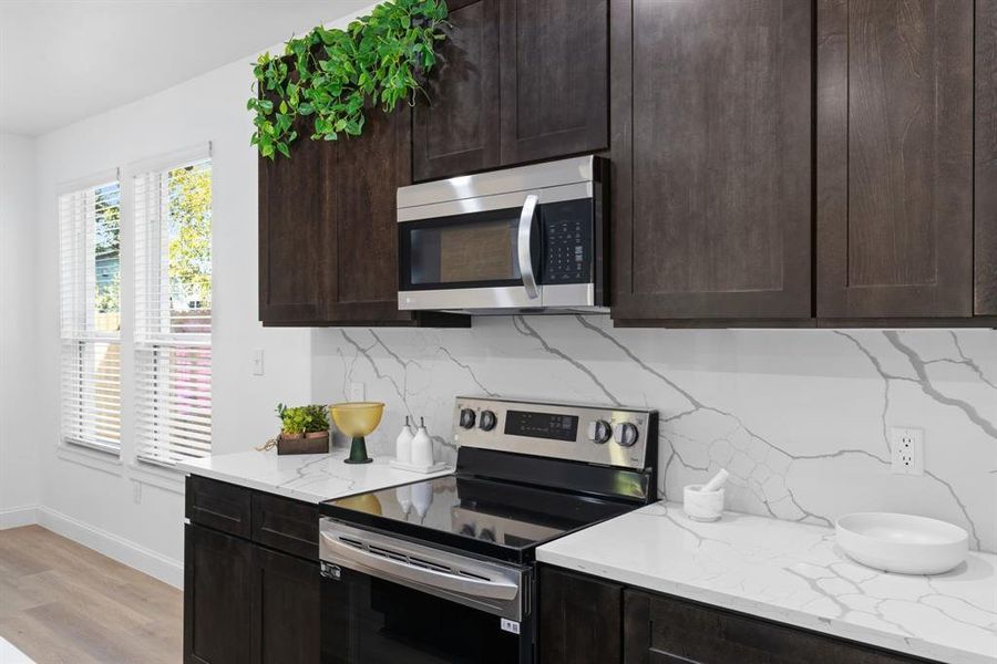 Kitchen featuring light stone counters, backsplash, light hardwood / wood-style flooring, dark brown cabinetry, and stainless steel appliances