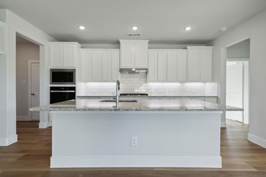 Kitchen with white cabinetry, hardwood / wood-style flooring, stainless steel appliances, and a center island with sink