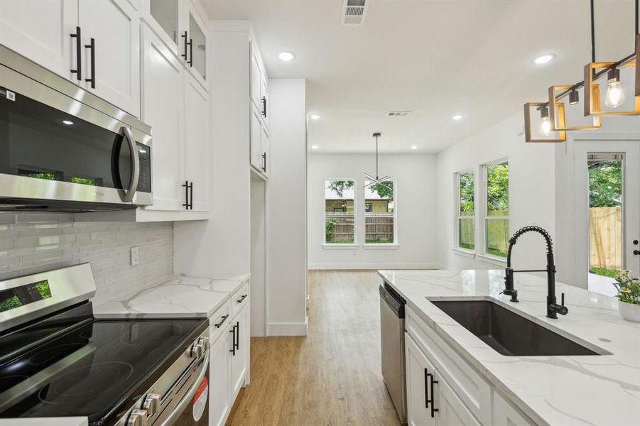 Kitchen with stainless steel appliances, light hardwood / wood-style floors, a wealth of natural light, and pendant lighting