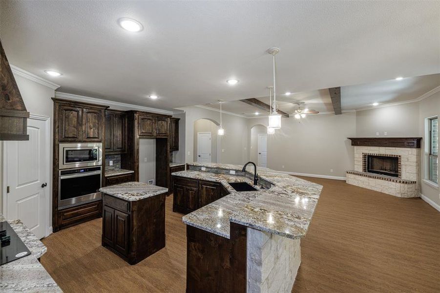 Kitchen with dark brown cabinetry, sink, a brick fireplace, a kitchen island with sink, and appliances with stainless steel finishes