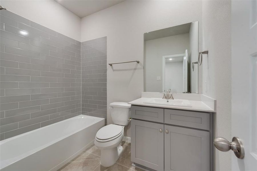 Full bathroom with vanity, tiled shower / bath combo, toilet, and tile patterned floors