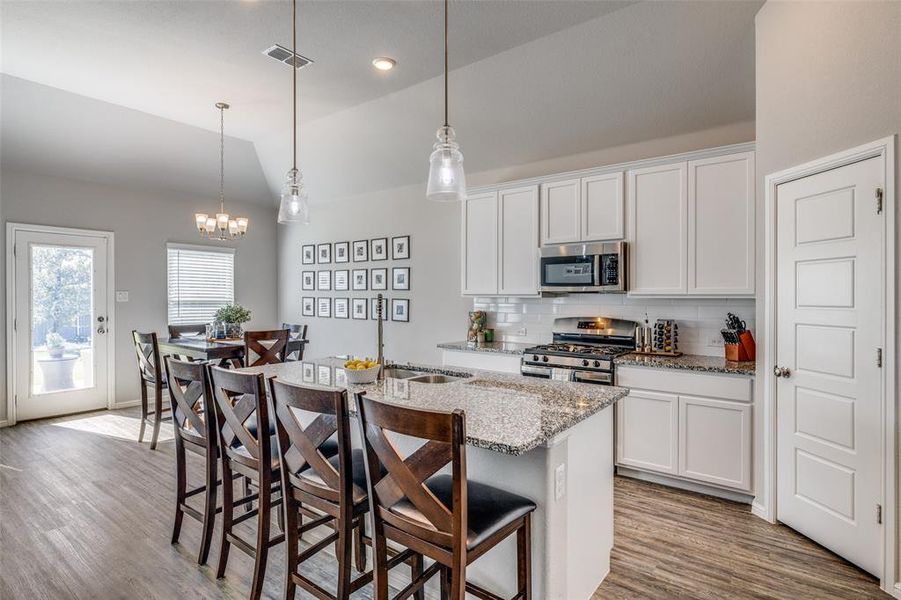 Kitchen featuring an island with sink, white cabinets, 11' sloped ceiling, a kitchen breakfast bar, and stainless steel appliances