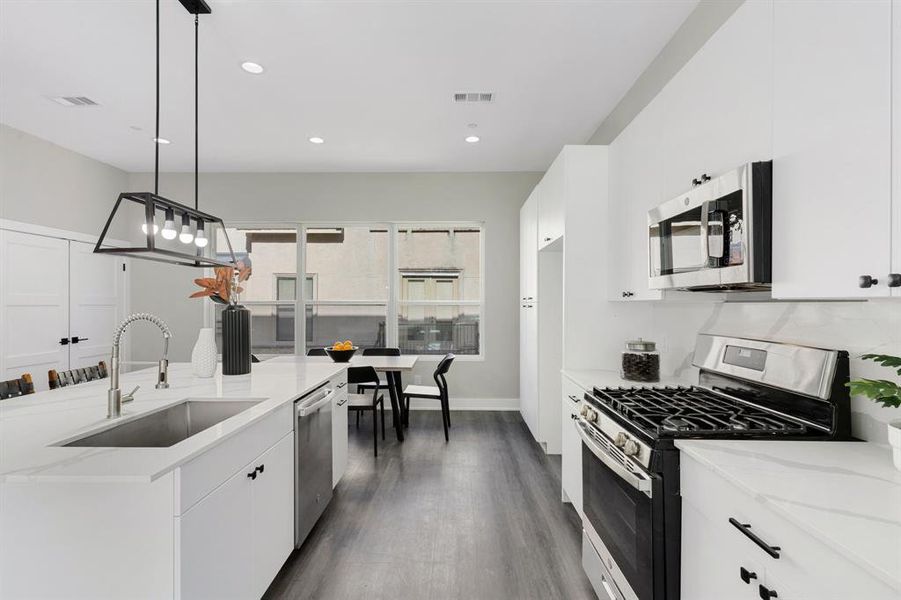 Kitchen with appliances with stainless steel finishes, sink, decorative light fixtures, dark hardwood / wood-style floors, and light stone countertops