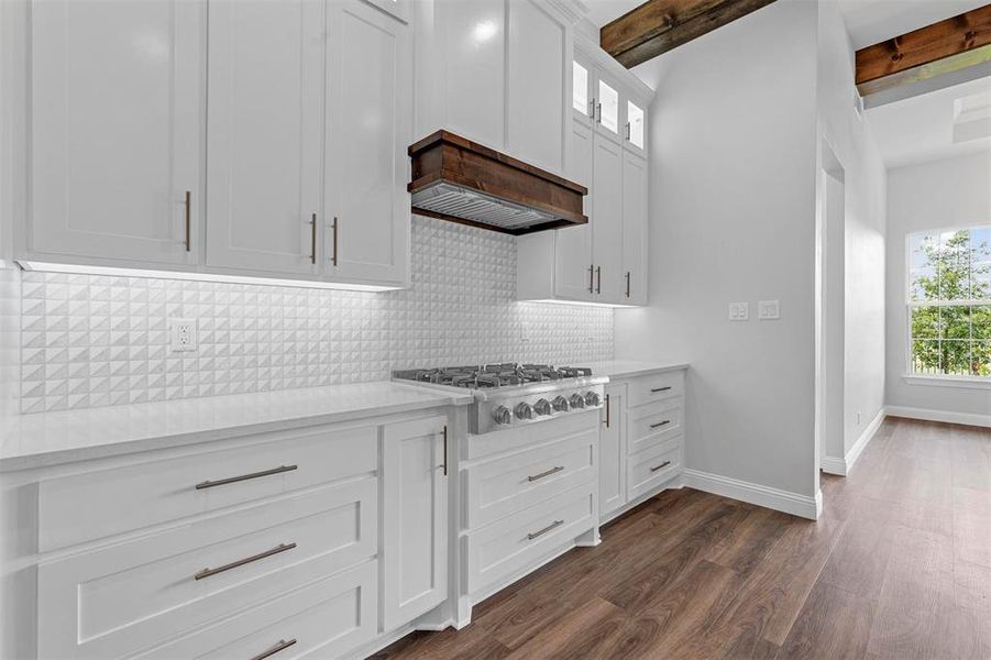 Kitchen featuring white cabinetry, dark wood-type flooring, beam ceiling, backsplash, and stainless steel gas cooktop
