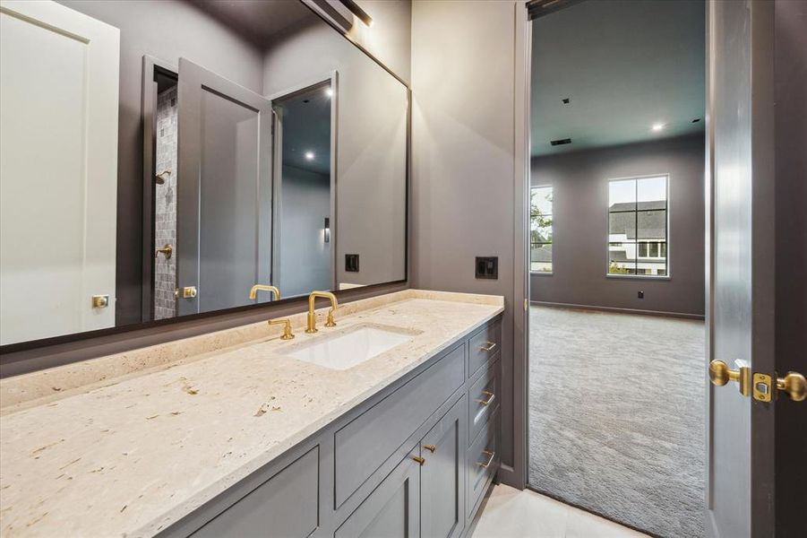 The guest bathroom includes modern dark cabinetry with brass fixtures, honed travertine countertop, and a full-length mirror. The bathroom connects to the media room for added convenience.