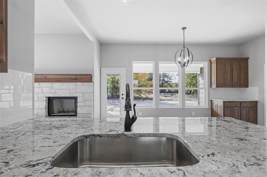 Kitchen featuring beamed ceiling, a chandelier, sink, light stone countertops, and a stone fireplace