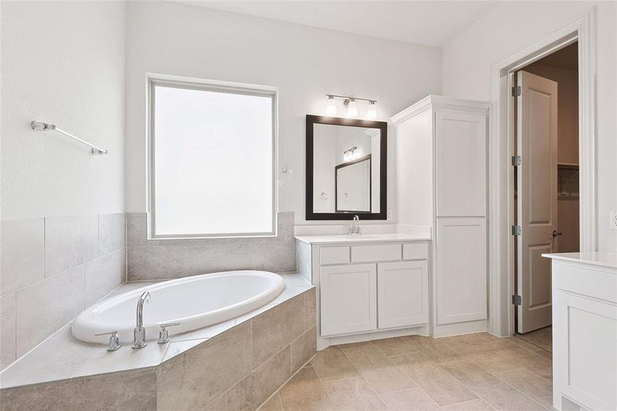 Bathroom featuring tiled tub, vanity, and tile floors