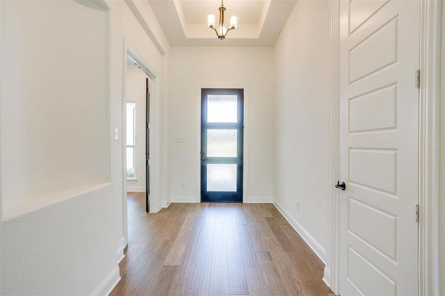 Foyer with light wood-type flooring, a raised ceiling, and a chandelier