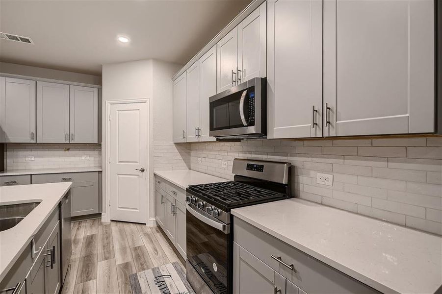Kitchen with light stone countertops, stainless steel appliances, light hardwood / wood-style flooring, and tasteful backsplash