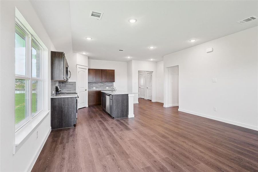 Kitchen with dark brown cabinets, a center island with sink, dark wood-type flooring, sink, and decorative backsplash