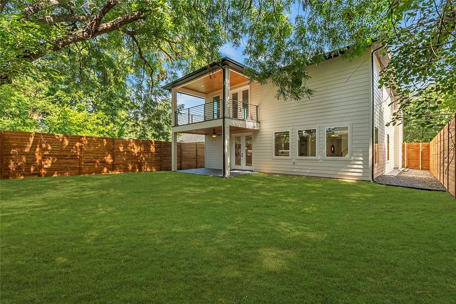 Rear view of house with a balcony, a patio area, and a lawn