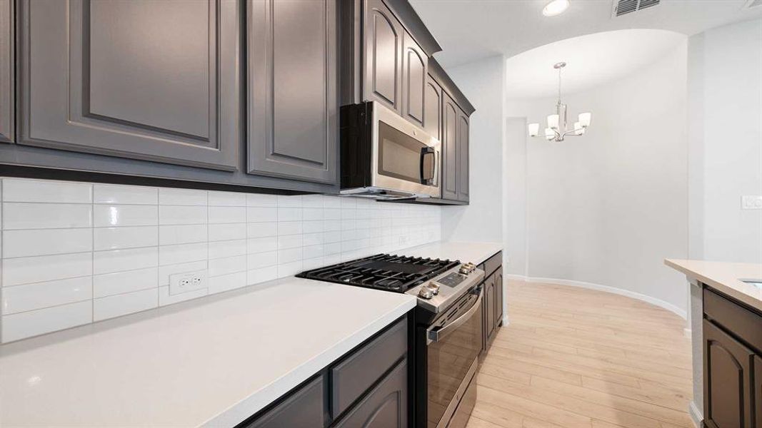 Kitchen featuring pendant lighting, backsplash, appliances with stainless steel finishes, a notable chandelier, and light wood-type flooring