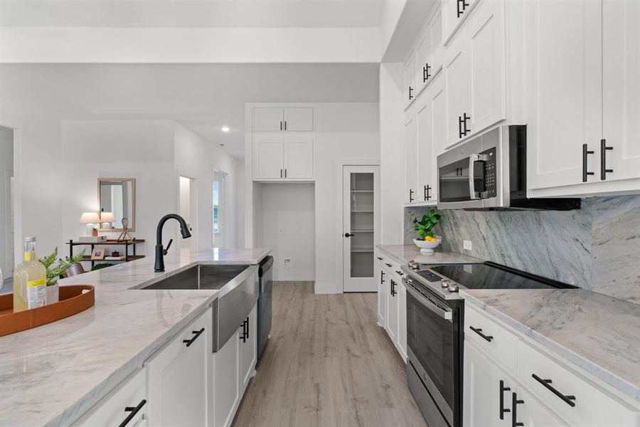 Kitchen featuring white cabinets, backsplash, appliances with stainless steel finishes, light stone countertops, and light hardwood / wood-style floors