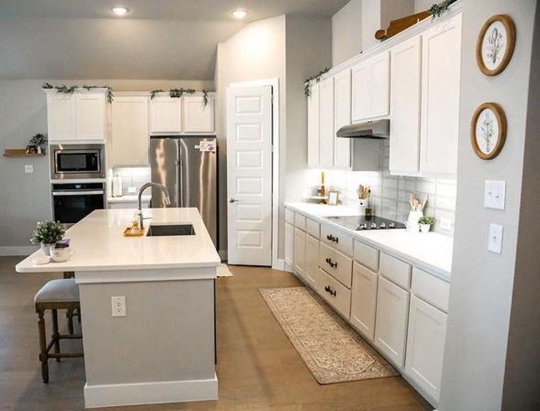 Kitchen featuring an island with sink, sink, stainless steel appliances, and white cabinets