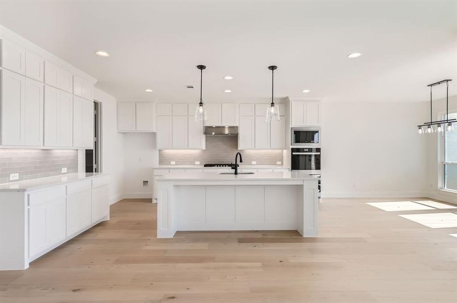 Kitchen with white cabinetry, black oven, a center island with sink, and hanging light fixtures