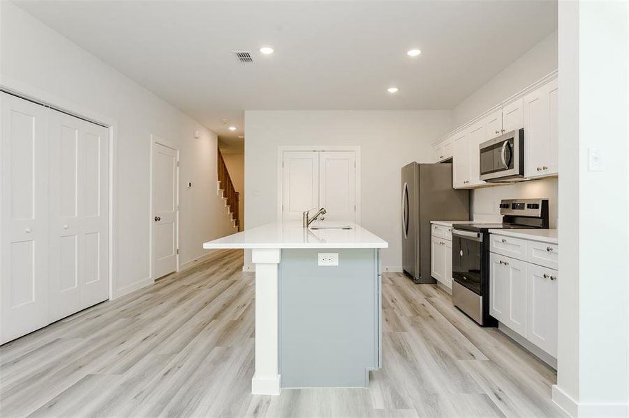 Kitchen with light hardwood / wood-style flooring, stainless steel appliances, a center island with sink, white cabinetry, and sink