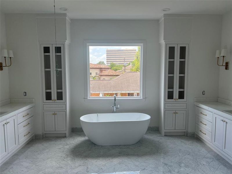 Primary bathroom with freestanding tub, dual vanities, marble floor and shower.